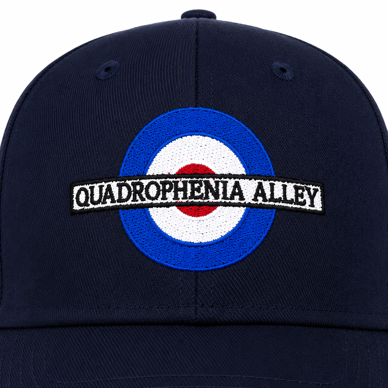 A close-up of a navy blue baseball cap featuring an embroidered roundel with blue, white, and red concentric circles and a black-and-white banner reading 'QUADROPHENIA ALLEY'.