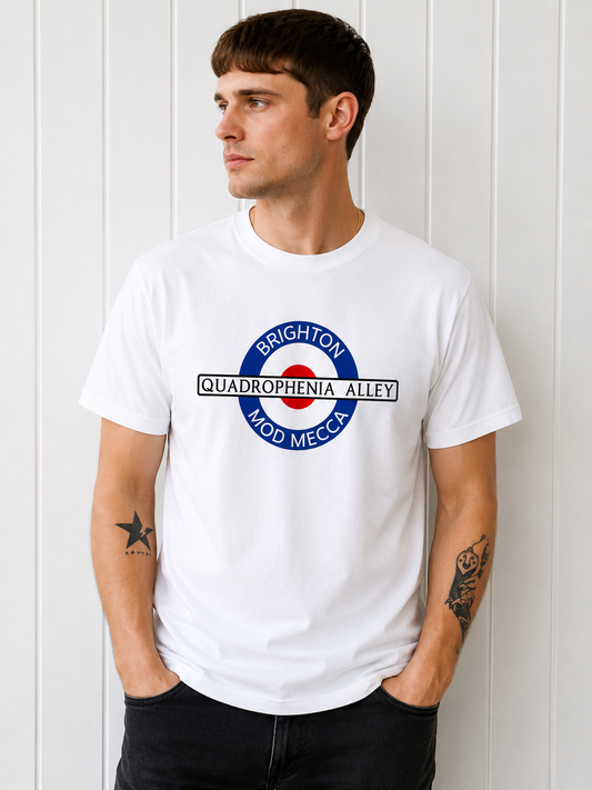 A man wearing a white short-sleeve t-shirt with a circular graphic on the chest that reads 'BRIGHTON QUADROPHENIA ALLEY MOD MECCA' in blue, red, and black, posed against a white paneled wall.